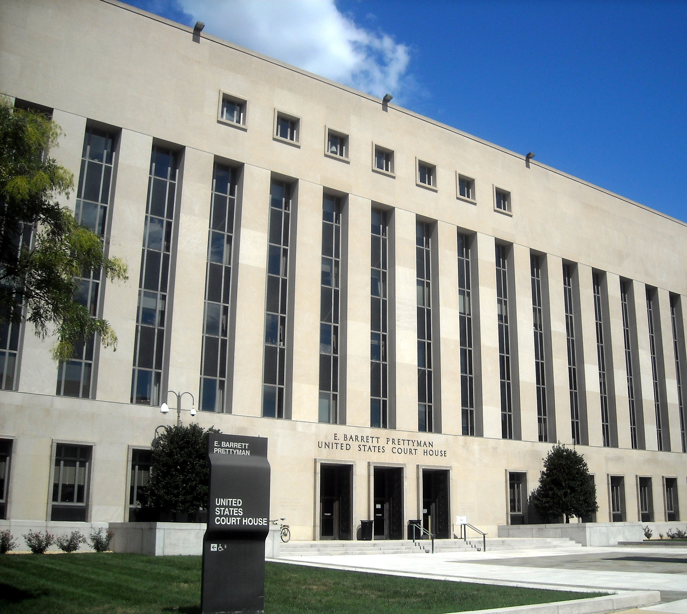 Pale stone facade of the E. Barrett Prettyman United States Court House in Washington, with tall narrow windows, a three-door entrance and a sign reading United States Court House.