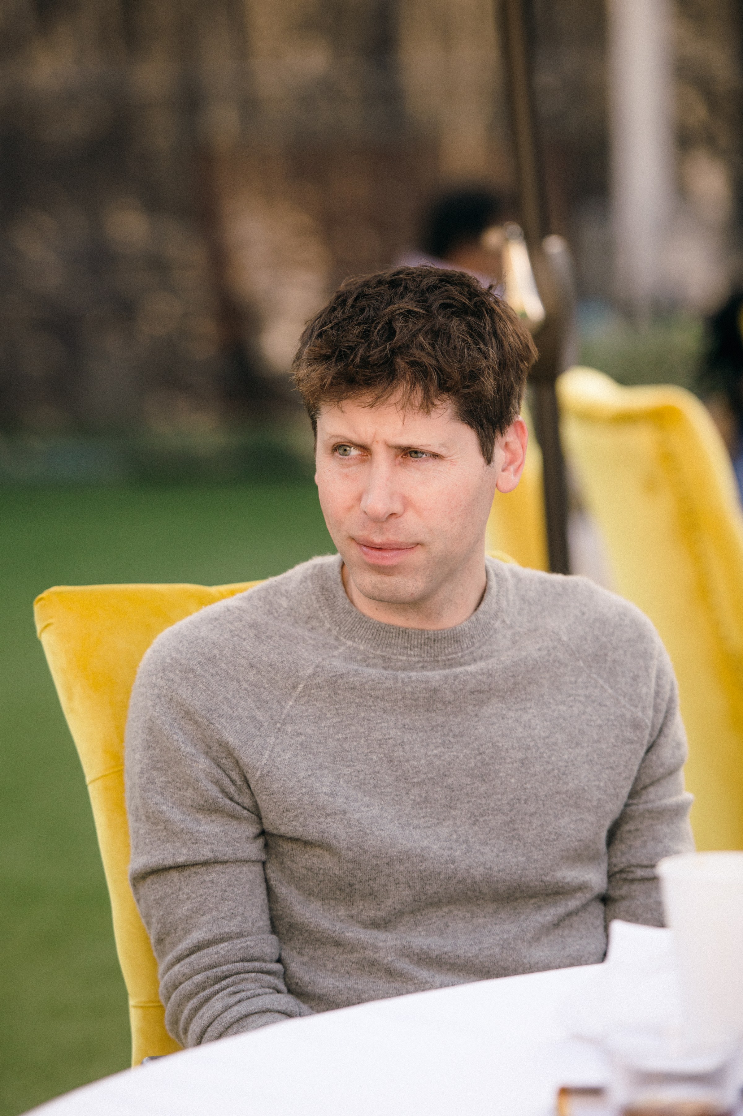 Sam Altman in a dark jacket, speaking on a stage at The Grove event.