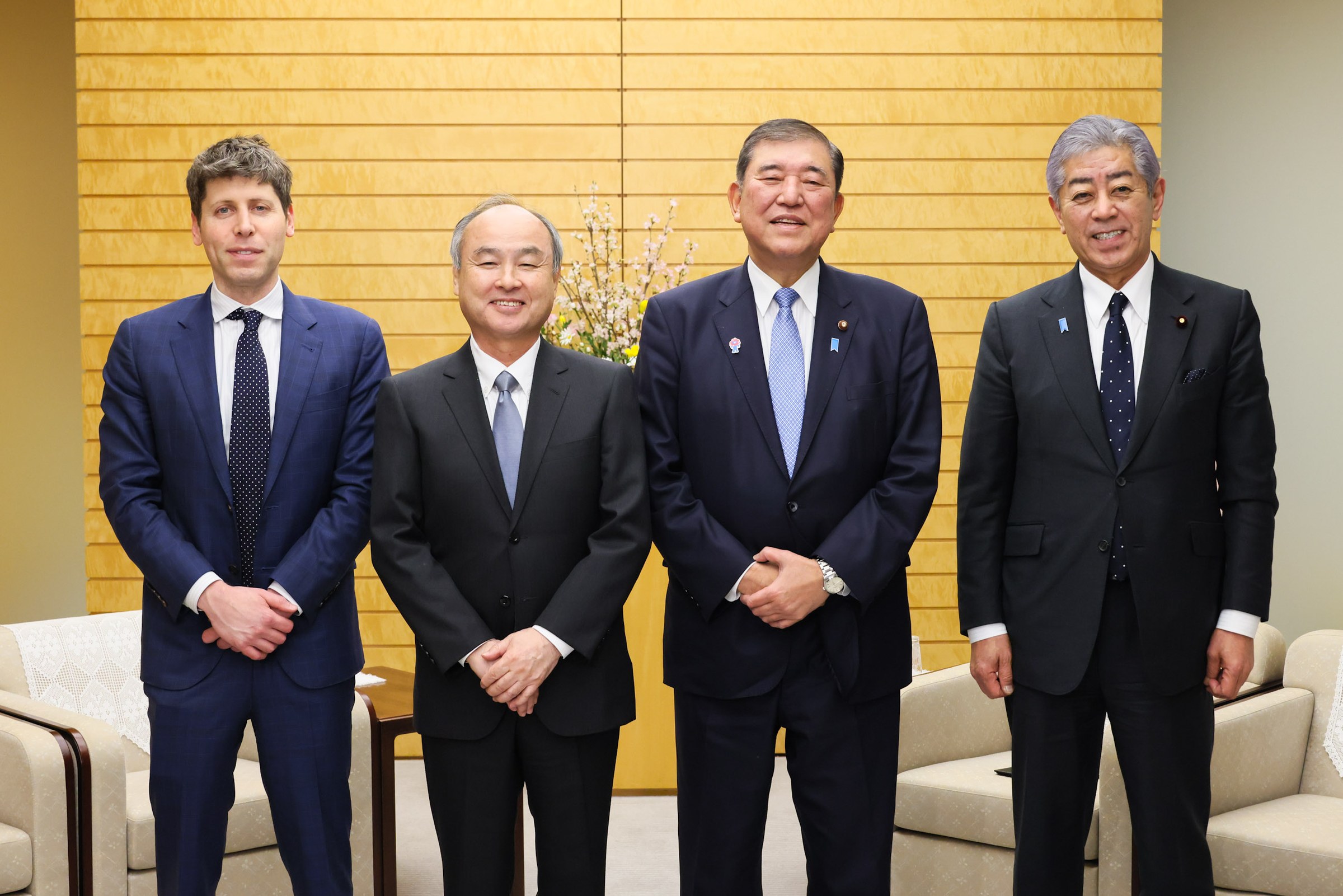Sam Altman stands with Masayoshi Son, Prime Minister Shigeru Ishiba and another man in front of a wood-panelled wall in Tokyo.