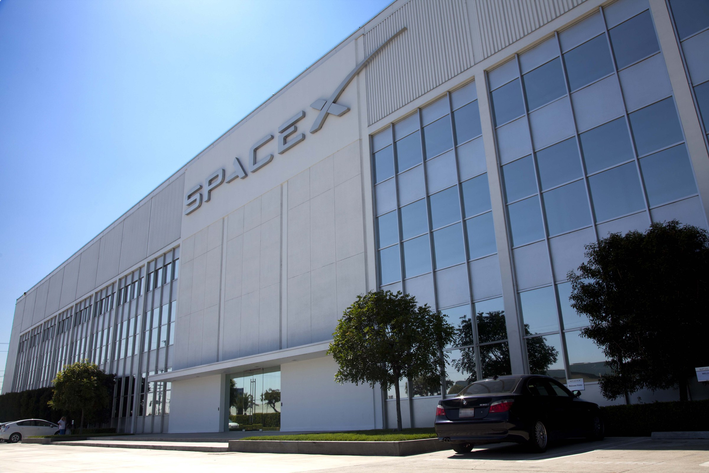 The SpaceX headquarters building in Hawthorne, California, with the company name in large letters on a white facade under a clear sky.