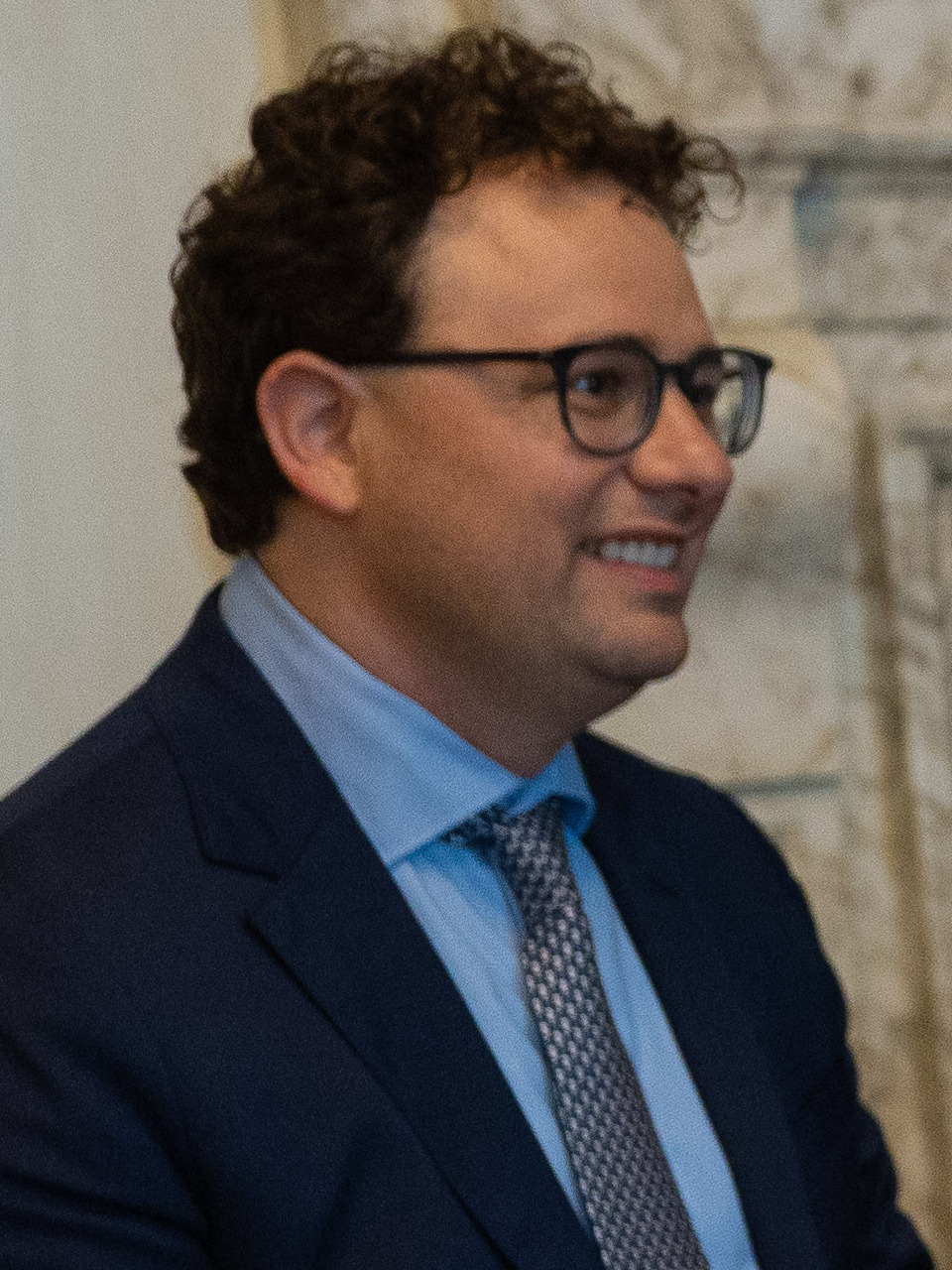 Dario Amodei, smiling, in a dark suit and patterned tie.